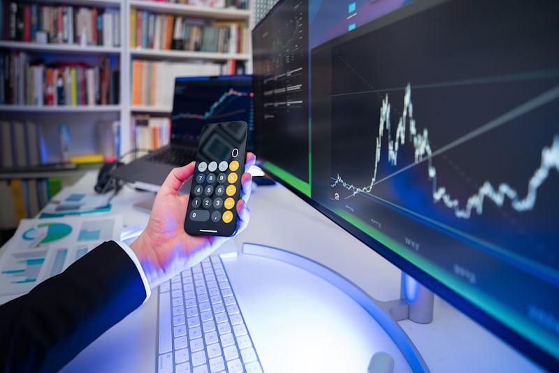 Hand holding calculator with stock market chart on computer screen,symbolizing smart finance and investment strategies.